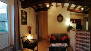 Una sala de estar acogedora con un sofá, una silla y una mesa de centro. Hay una chimenea, un reloj en la pared y una ventana.