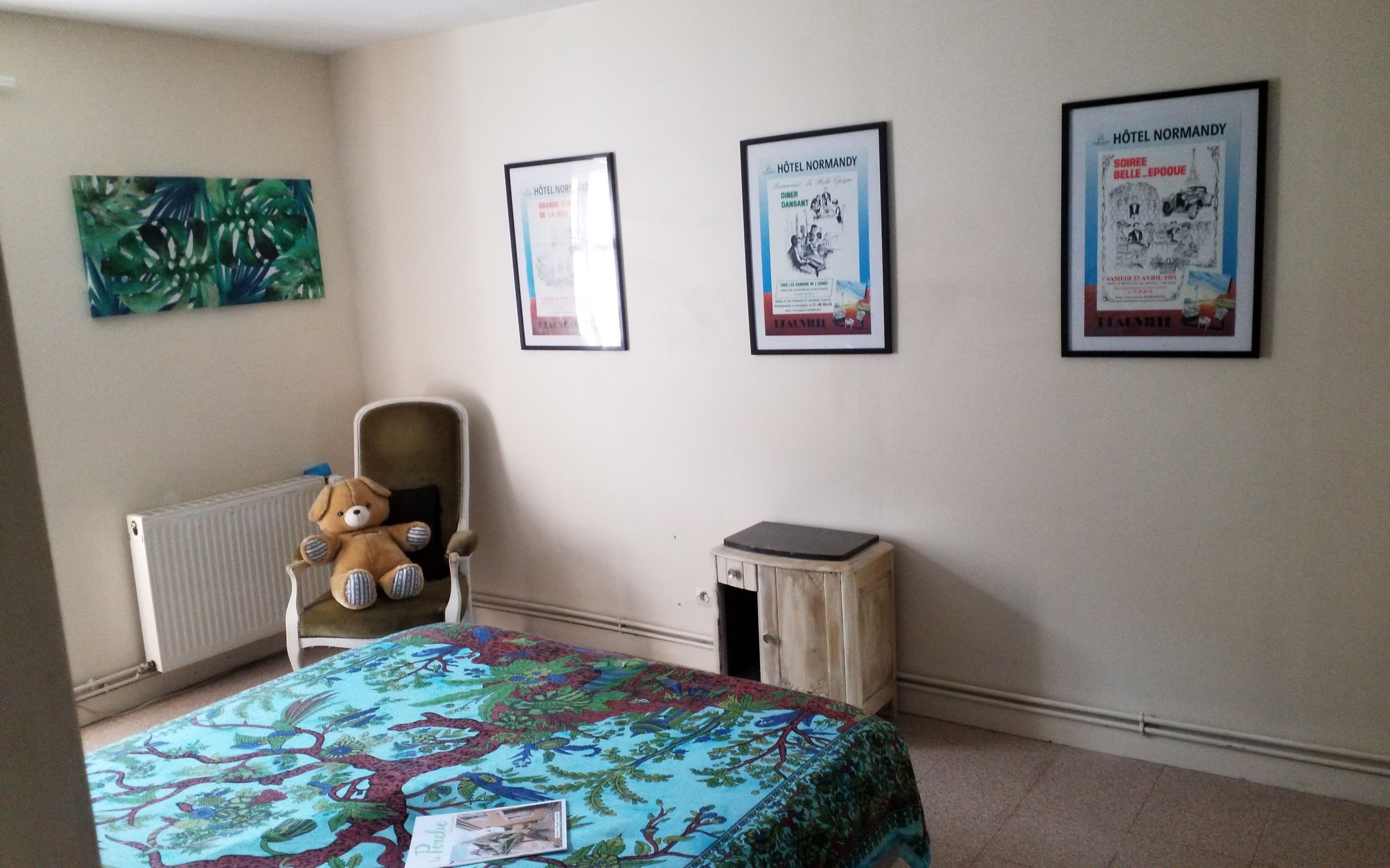 A bedroom with a bed, a chair, a radiator, and three framed posters on the wall.