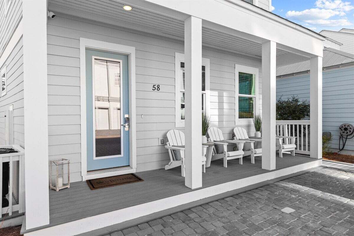 Ett vitt hus med en blå dörr och husnummer 58. På verandan står vita stolar och ett bord.