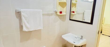 Un baño con inodoro, lavamanos y espejo. Hay un perchero y un cubo de basura pequeño.