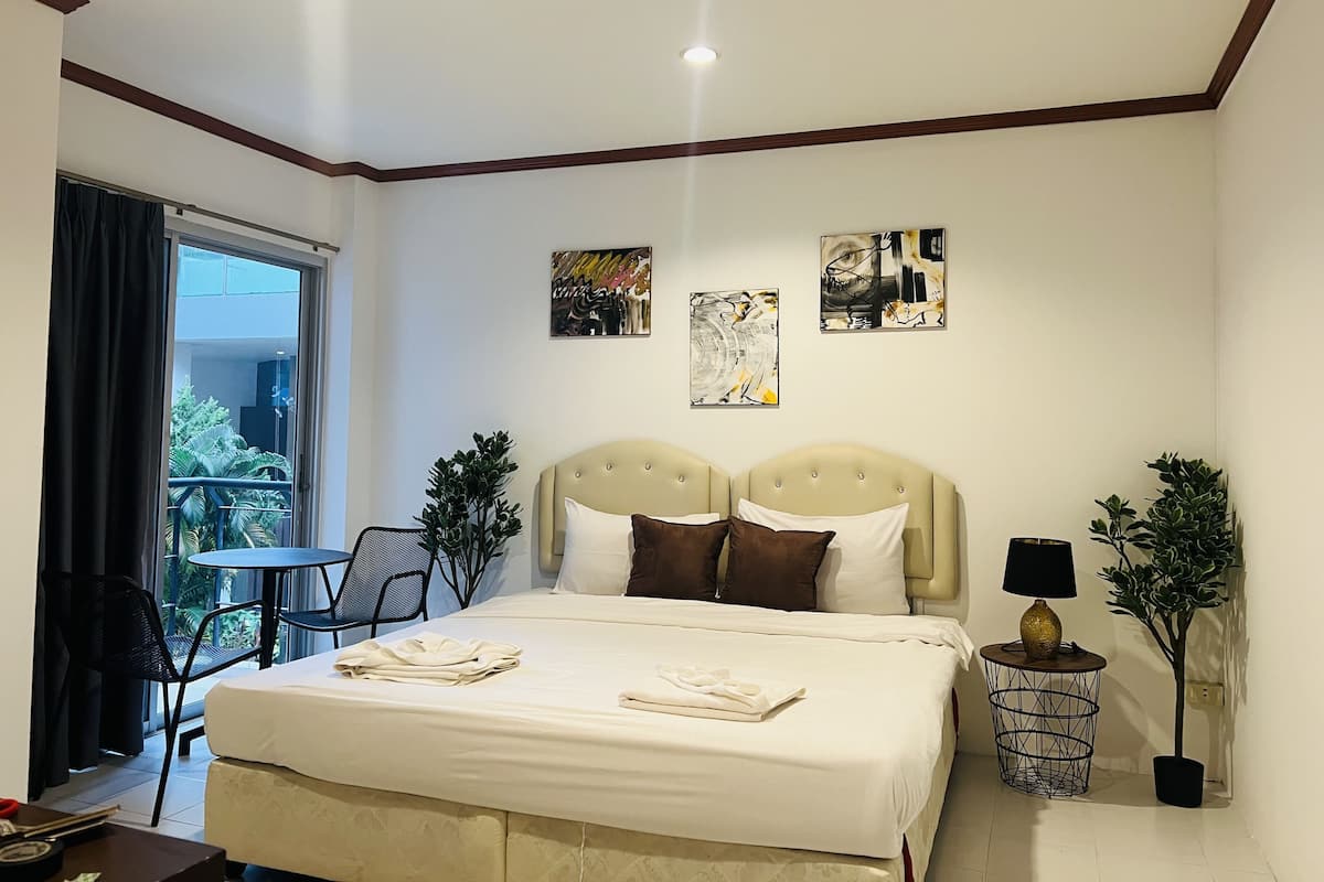 A hotel room with a bed, two side tables, a chair, a small table, and a balcony with a view.