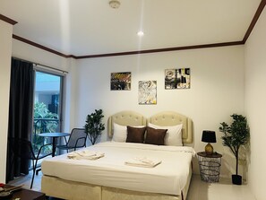 A hotel room with a bed, two side tables, a chair, a small table, and a balcony with a view. - Omaya Guest House (Patong)