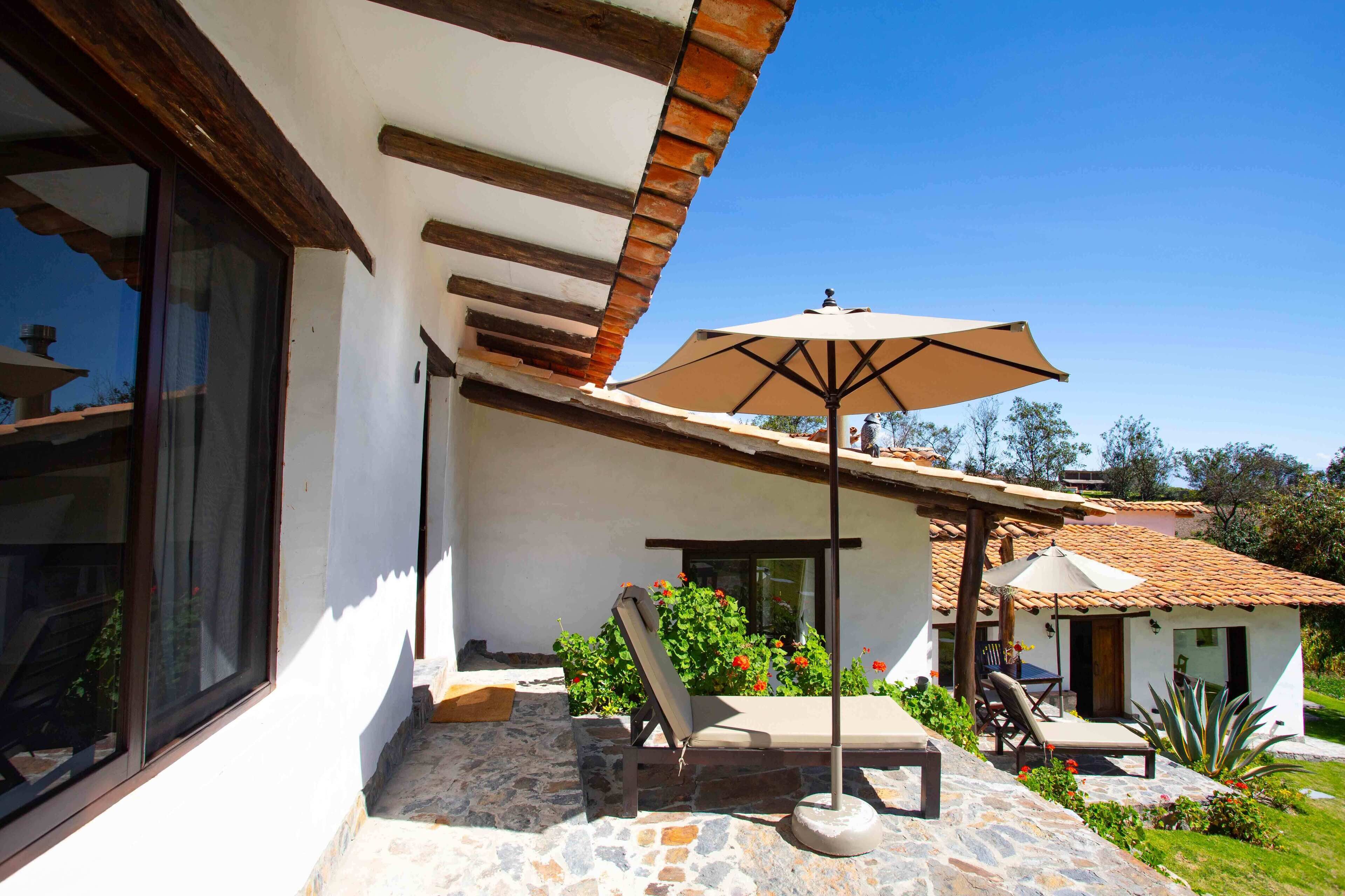 Eine Terrasse mit Liegestuhl und Sonnenschirm, ein Steinboden und ein kleiner Garten mit roten Blumen.