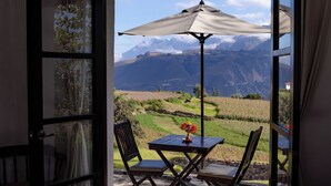 Una habitación con cama, una mesa con sillas y vistas a las montañas desde una puerta abierta.