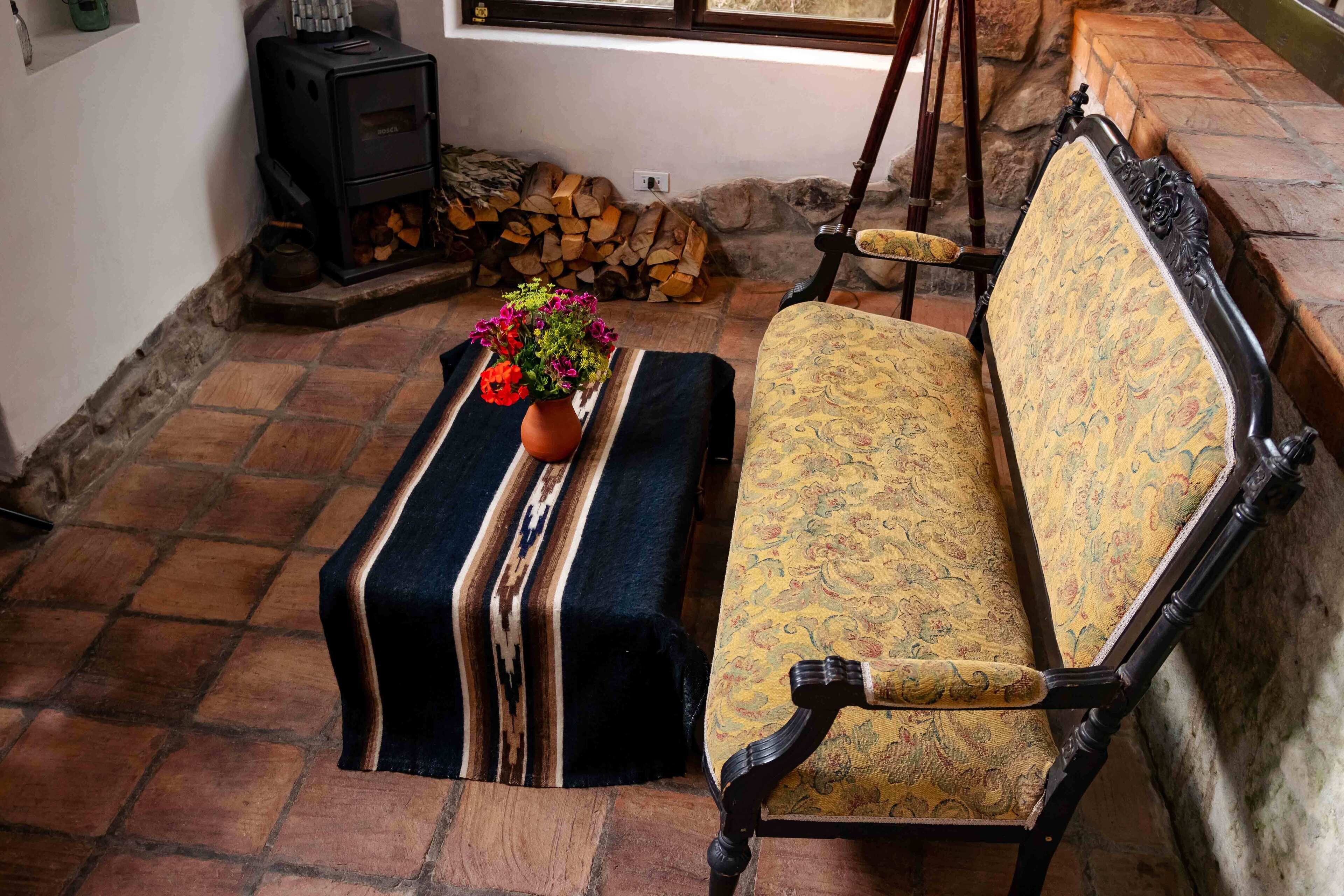 A cozy room with a bench, a table with a vase of flowers, a fireplace, and a chair.