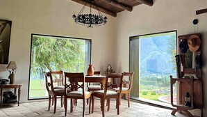 Un comedor con sillas de madera y una mesa, ventanas amplias con vistas a la vegetación, y un candelabro.