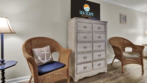 A room with a wicker chair, a dresser, and a wall-mounted sign reading "SEA SCAPE PROPERTIES". - Studio w/Marina Views & Pool! Walk to Waterfront Dining! (Wrightsville Beach)