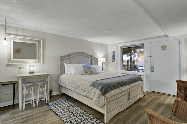 A bedroom with a bed, bedside table, lamp, and a view of the outside.