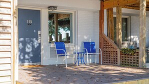 A porch with two blue chairs and a small table, a wooden staircase, and a door marked with the number 115. - Studio w/Marina Views & Pool! Walk to Waterfront Dining! (Wrightsville Beach)