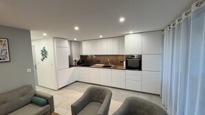 A modern kitchen with white cabinets, a built-in oven, and a dining area with two grey chairs.