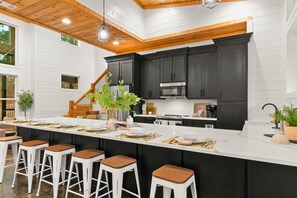 Cozinha moderna com armários escuros, uma ilha grande com banquetas e teto de madeira.