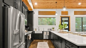 Una cocina moderna con refrigerador de acero inoxidable, gabinetes negros, encimera blanca y techo de madera.
