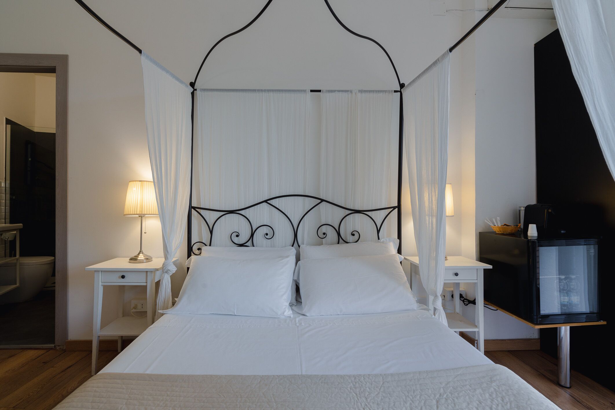 A neatly made bed with a canopy, two bedside tables with lamps, and a television on a stand.