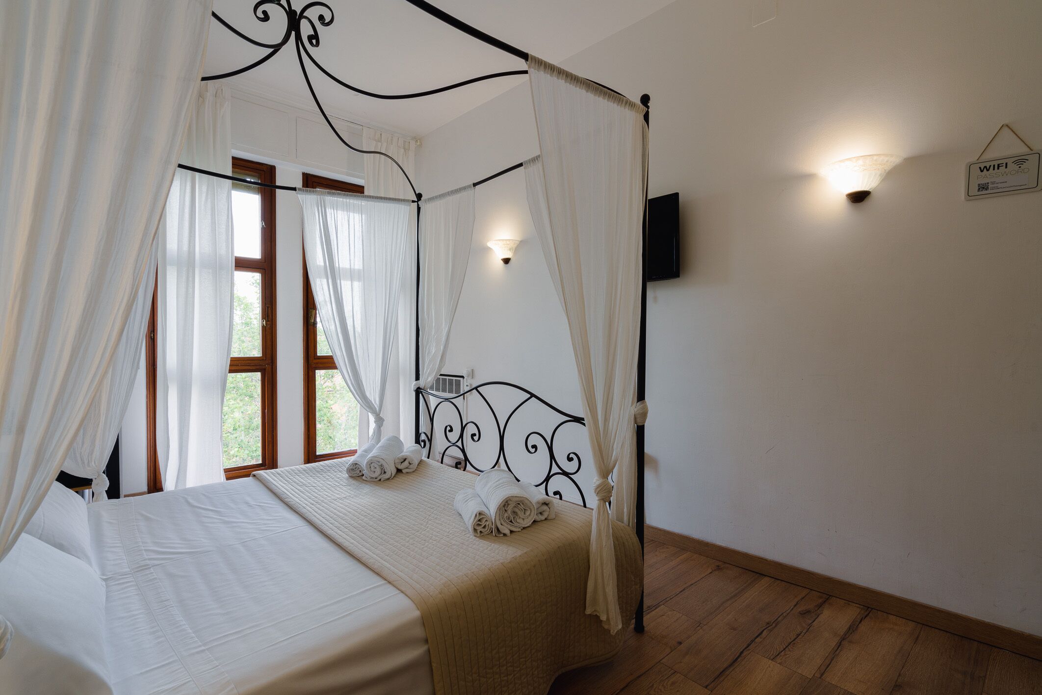 Un letto rifatto con tenda, una TV a parete e un cartello che indica la disponibilità del WiFi.