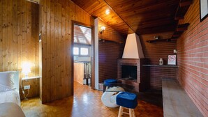 Un interior de madera con chimenea, una cama y una mesa de vidrio con taburetes.