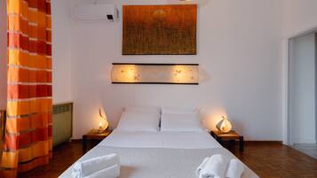 Ein Hotelzimmer mit einem großen Bett, zwei Nachttischen inklusive Lampen, einer Wand-Klimaanlage und einem großen, abstrakten Gemälde über dem Bett.