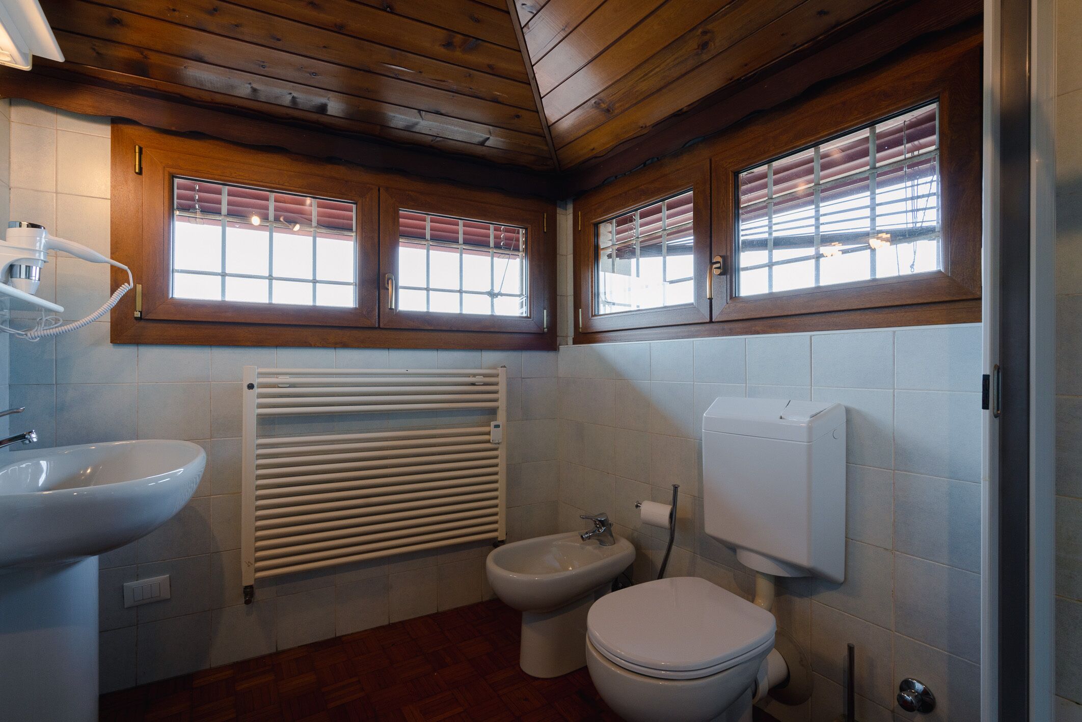 Une salle de bain avec un plafond en bois, un lavabo, un bidet, des toilettes et un radiateur.