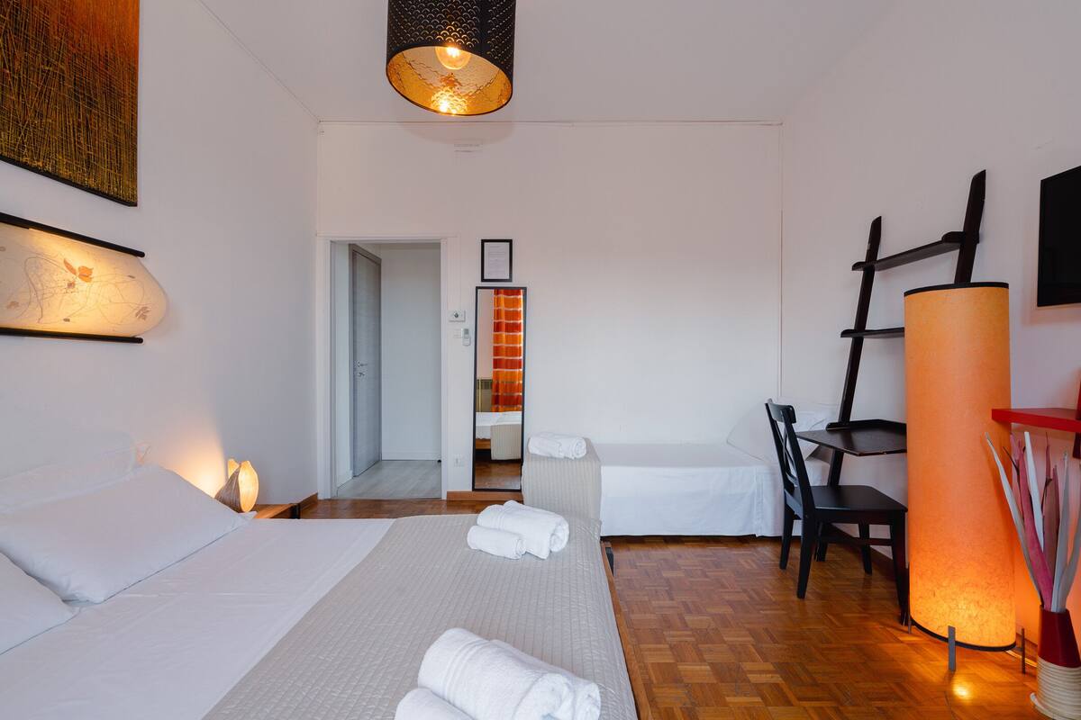 Una habitación de hotel con cama, escritorio, silla, lámpara y un cuadro en la pared.