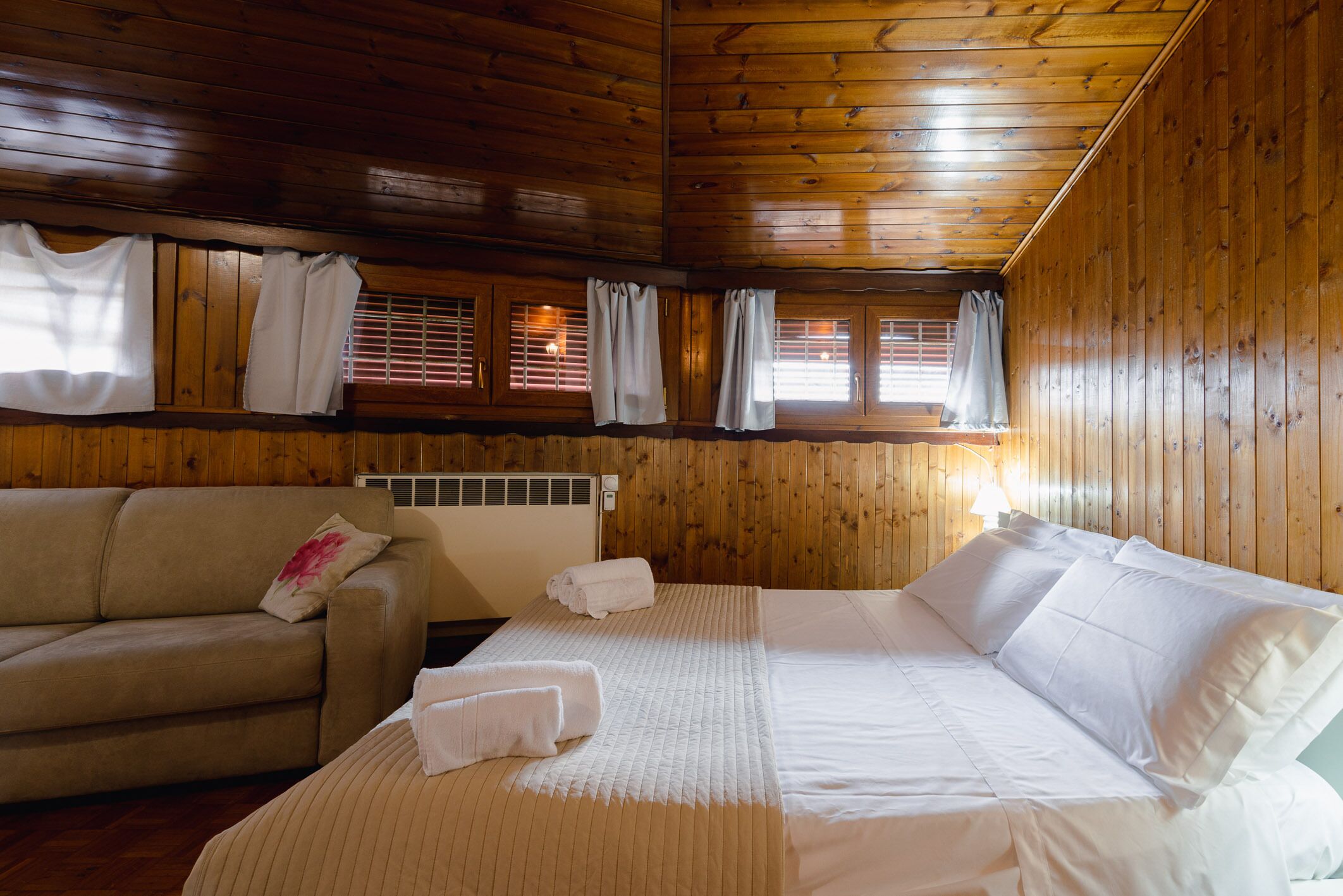 A wooden-paneled room with a bed, a sofa, and a window with blinds.