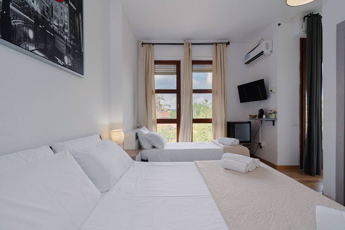 Una habitación de hotel con dos camas, televisión, aire acondicionado y ventana con cortinas.