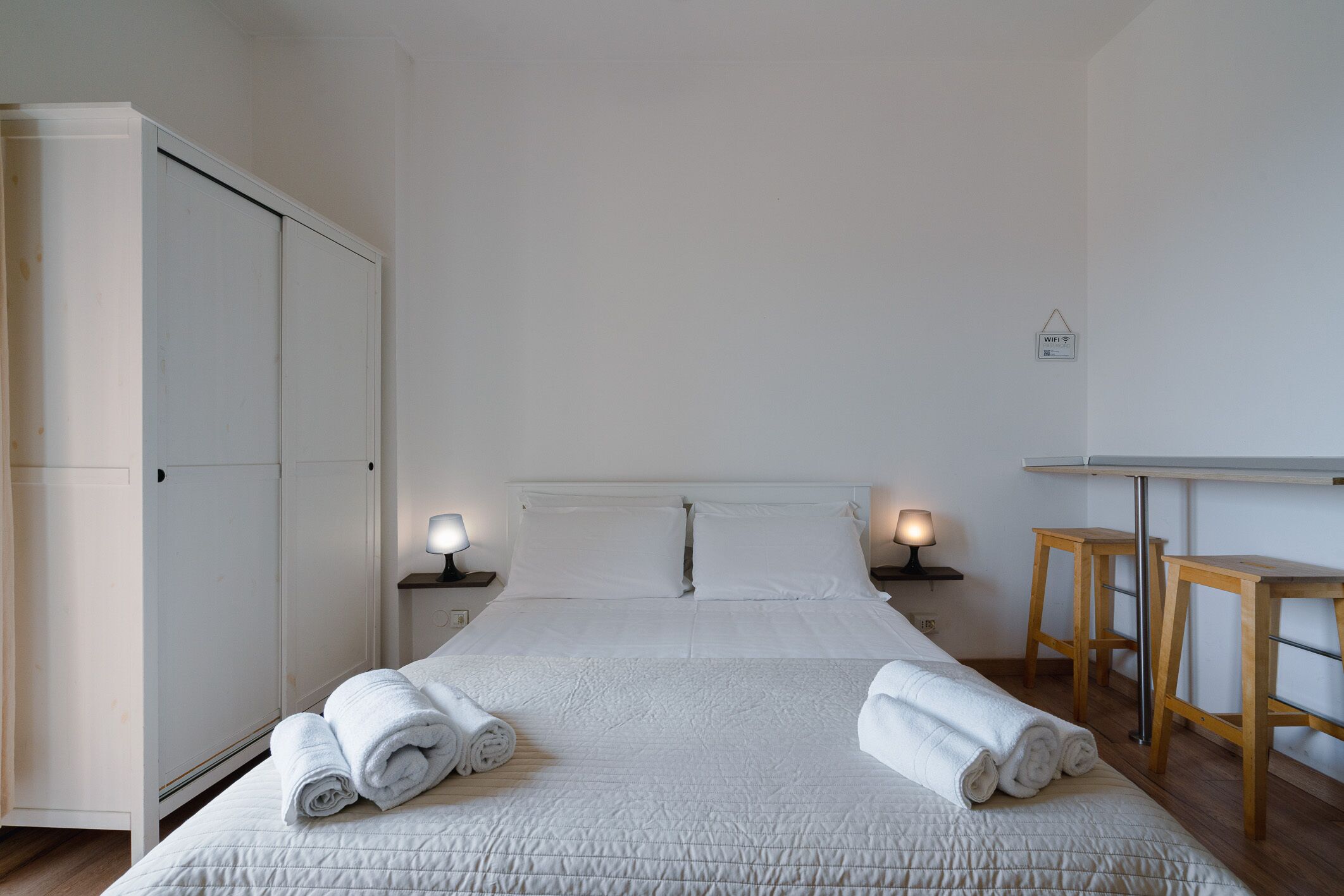 Ein Hotelzimmer mit einem Bett, zwei Nachttischlampen, einem Holztisch und einem Kleiderschrank.