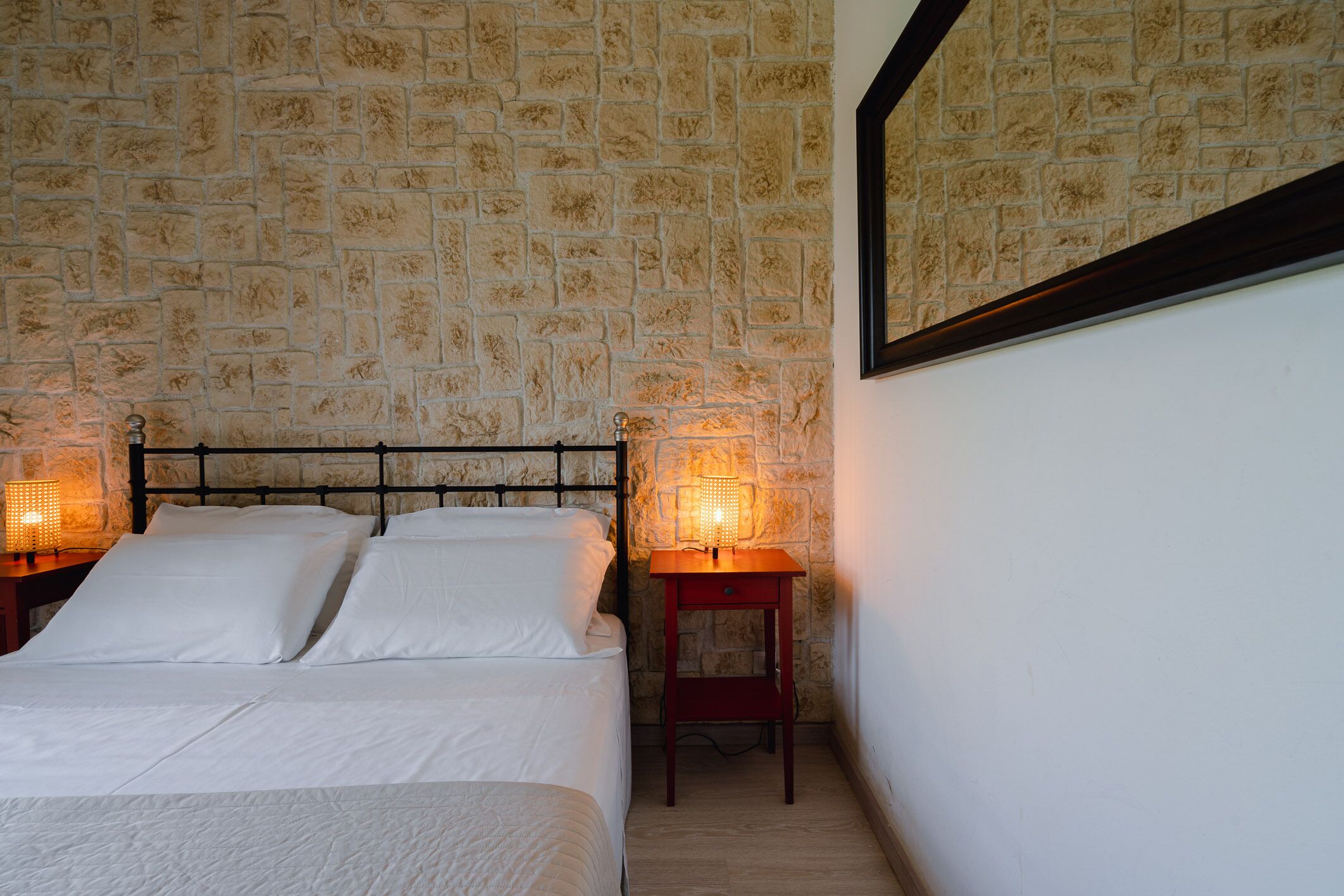 Ein Schlafzimmer mit Wand im Stein-Look, einem Bett mit weißer Bettwäsche und zwei Nachttischlampen.