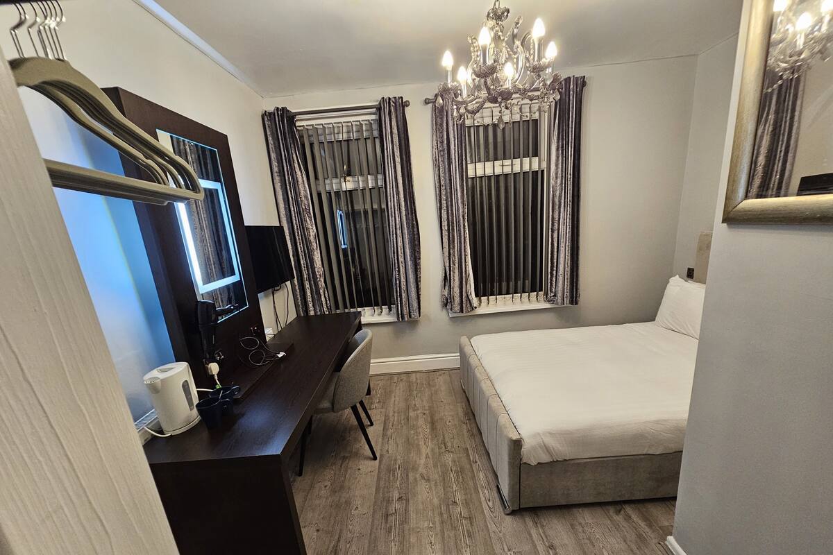 Un dormitorio con una cama, un escritorio con ordenador, un televisor y una araña.
