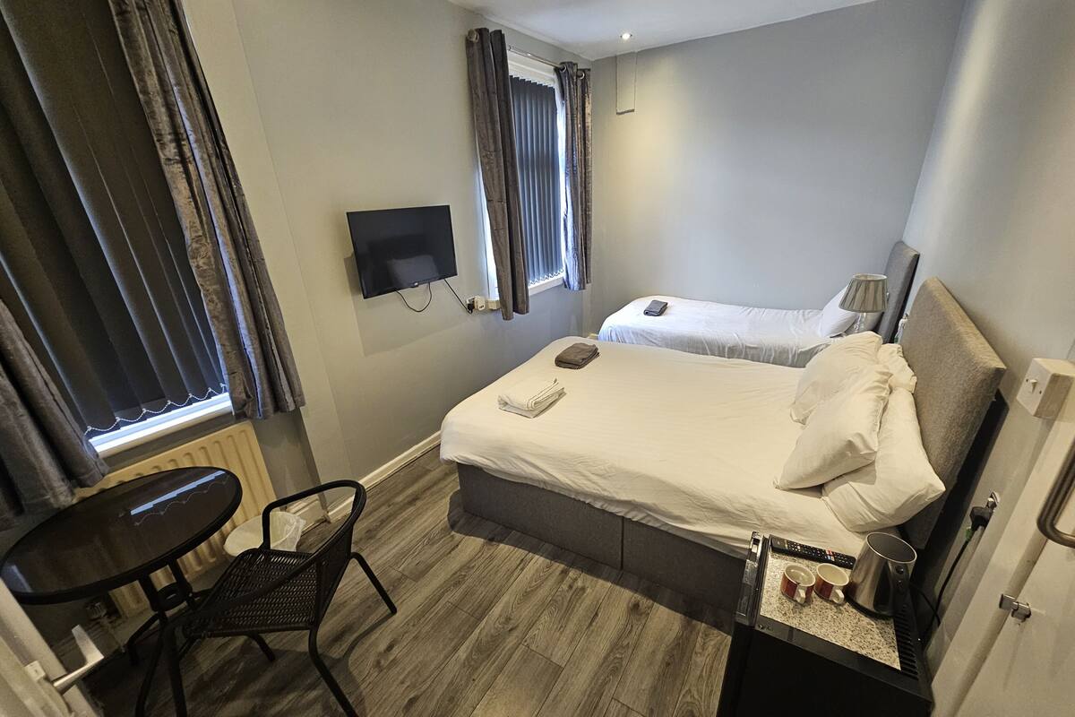 Habitación de hotel con cama, escritorio, silla, televisión y ventana con cortinas.