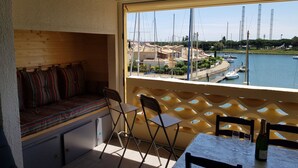 Un balcone con vista su una marina, una zona relax con una panchina e sedie, e un tavolo con bicchieri e una bottiglia.