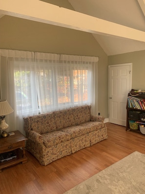 A living room with a floral sofa, a lamp, a bookshelf, and a door. - Blissful Vacation Experience! Spacious, fully fenced house with backyard oasis! (Yarmouth)