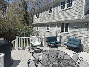 A covered deck with outdoor furniture, including a white rocking chair, two blue chairs, and a blue sofa. - Blissful Vacation Experience! Spacious, fully fenced house with backyard oasis! (Yarmouth)