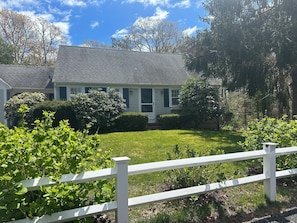 A house with a well-maintained lawn and a white fence in the foreground. - Blissful Vacation Experience! Spacious, fully fenced house with backyard oasis! (Yarmouth)
