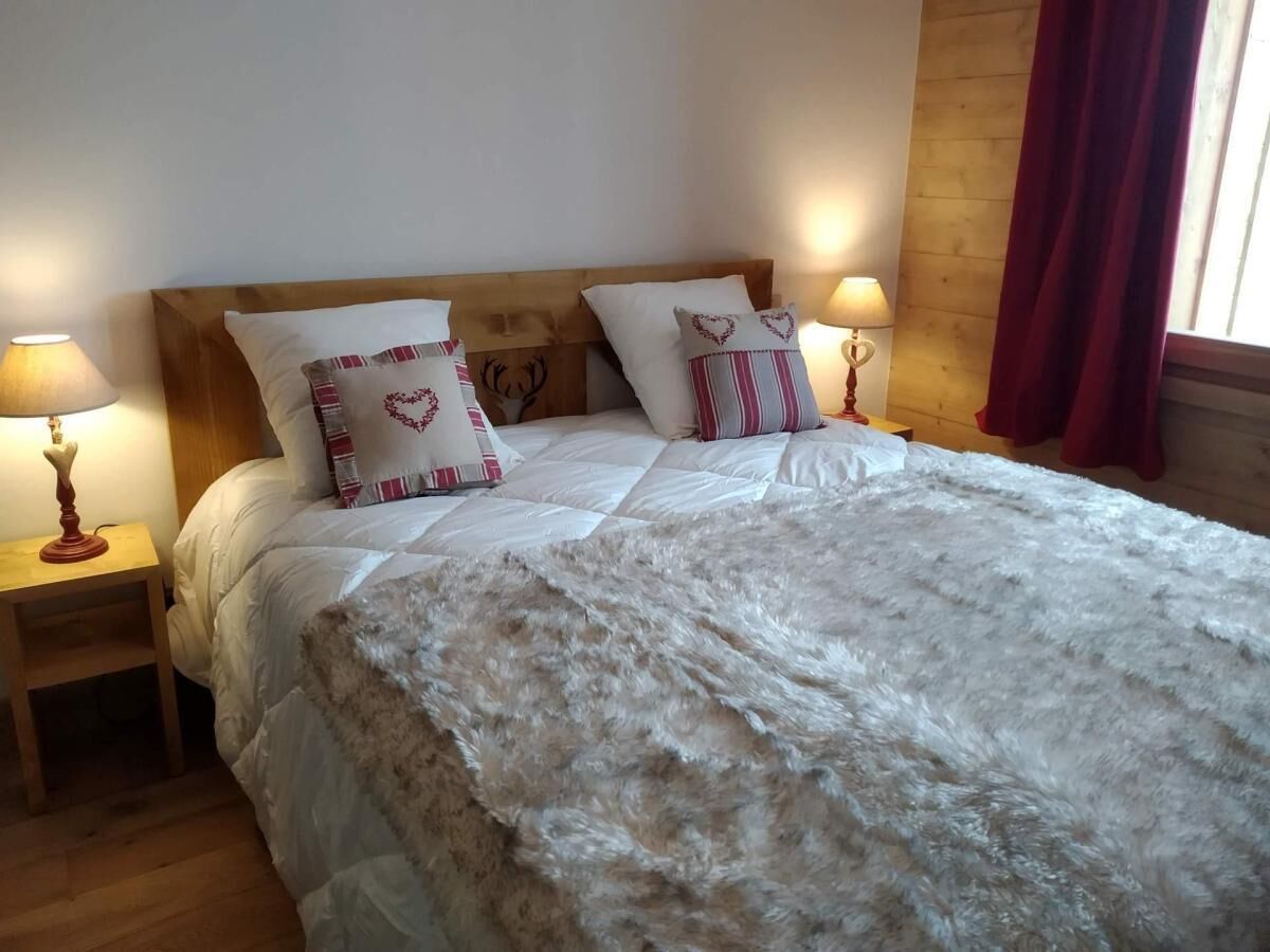 A neatly made bed with a fluffy white blanket, two heart-shaped pillows, and a wooden headboard. There are two bedside tables with lamps, one on each side of the bed.