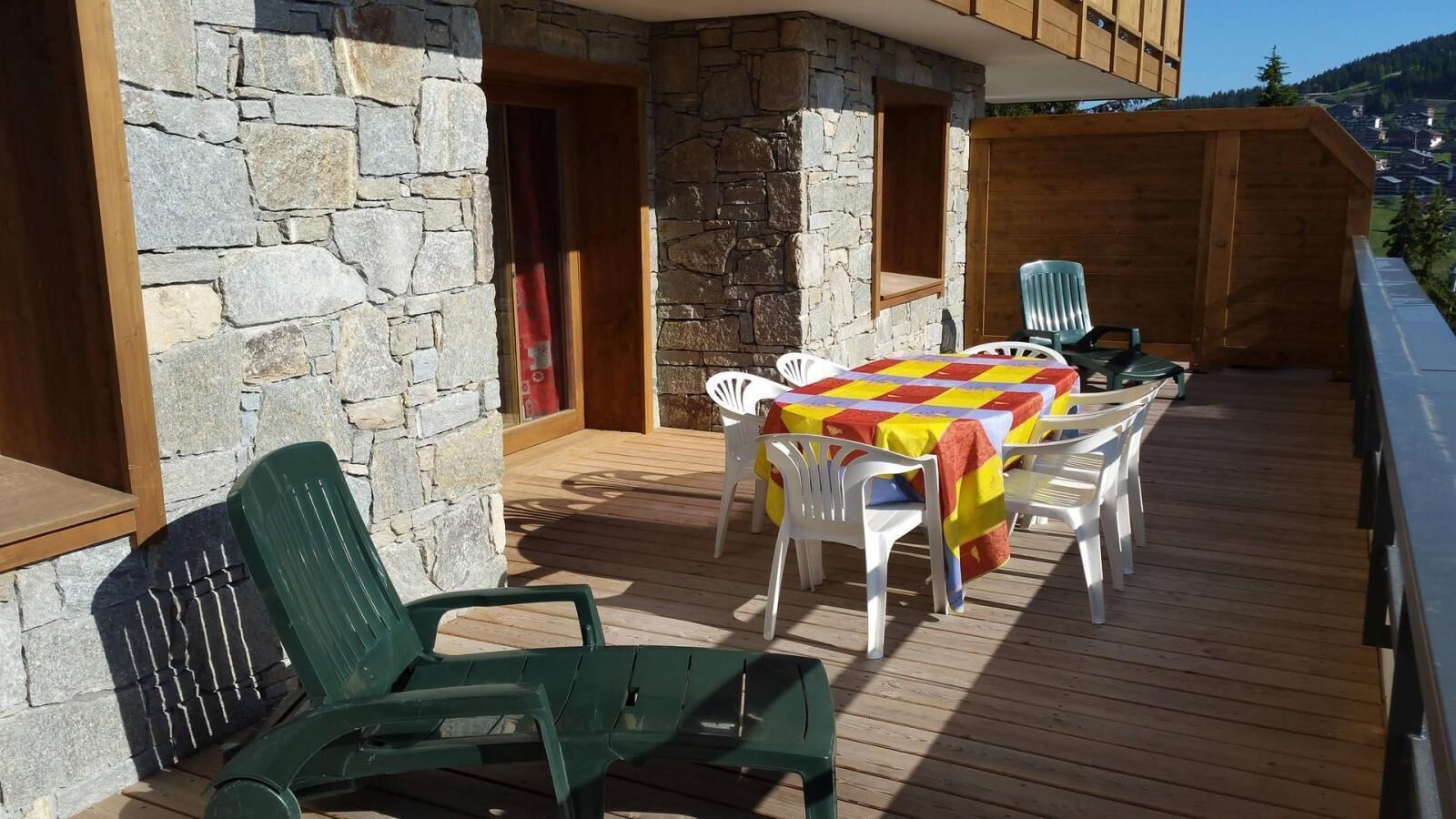 Une terrasse en bois avec un muret en pierre, des sièges d’extérieur et une table recouverte d’une nappe colorée.