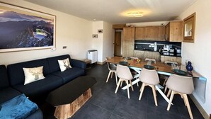 A modern living room with a dark-colored sofa, a wooden coffee table, and a dining area with a wooden table and chairs. - 250m from ski slopes, Ground floor, terrace, parking, tv, ski locker, 72m², Les Saisies (Villard-sur-Doron)