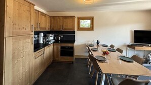 A modern kitchen with wooden cabinets, a dining area with a table set for four, and a large window providing natural light. - 250m from ski slopes, Ground floor, terrace, parking, tv, ski locker, 72m², Les Saisies (Villard-sur-Doron)