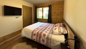 A bedroom with a bed, a TV mounted on the wall, a window with curtains, and wooden paneling on the walls. - 250m from ski slopes, Ground floor, terrace, parking, tv, ski locker, 72m², Les Saisies (Villard-sur-Doron)