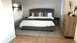 A modern bedroom with a large bed, a grey headboard, a wooden dresser, and a rug.