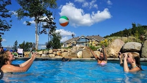 Un espace piscine avec un ballon de plage en l’air, entouré de rochers et d’arbres.