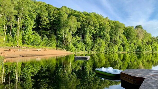 A calm lake with a dock, a boat, and a forested hillside.
