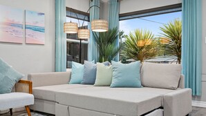 A modern living room with a beige sofa, light blue cushions, and a woven pendant light.