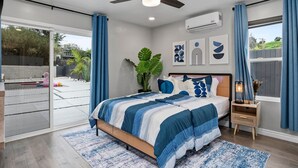 A bedroom with a bed, a nightstand, a ceiling fan, a window with curtains, and a view of the outside.