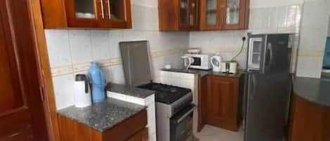 Una cocina con gabinetes de madera, una estufa a gas, un horno, un microondas y un refrigerador.