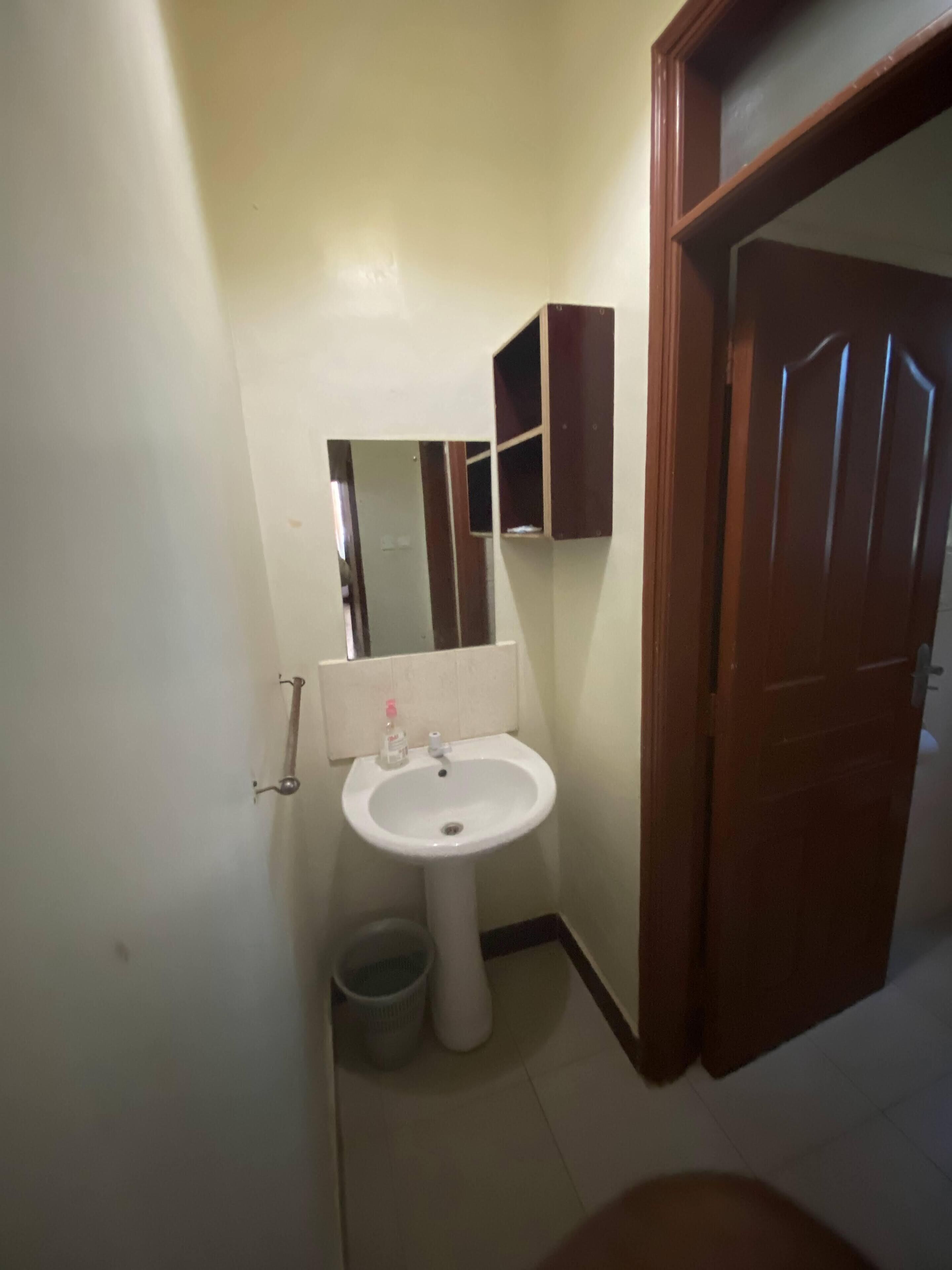 A small bathroom with a white sink, a mirror, and a wooden door.
