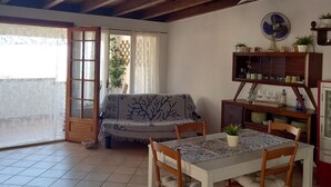 A dining area with a table, chairs, and a ceiling fan. There is a sofa and a window with curtains. - Attic room with terraces facing the sea, close to the beach and Scala dei Turchi (Lido Rossello)