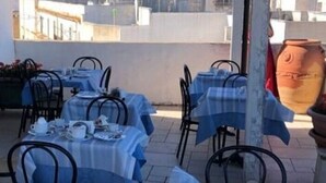 An outdoor dining area with tables covered in blue tablecloths and black metal chairs.