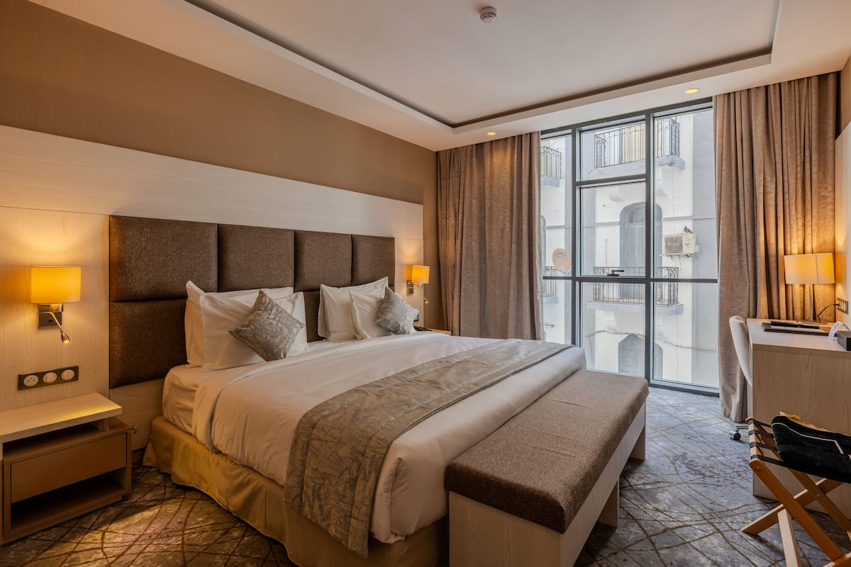 A hotel room with a large bed, bedside lamps, a desk, and a view through the window.