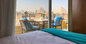 Habitación de hotel con cama, dos sillones de mimbre, una mesita y vista a las pirámides.
