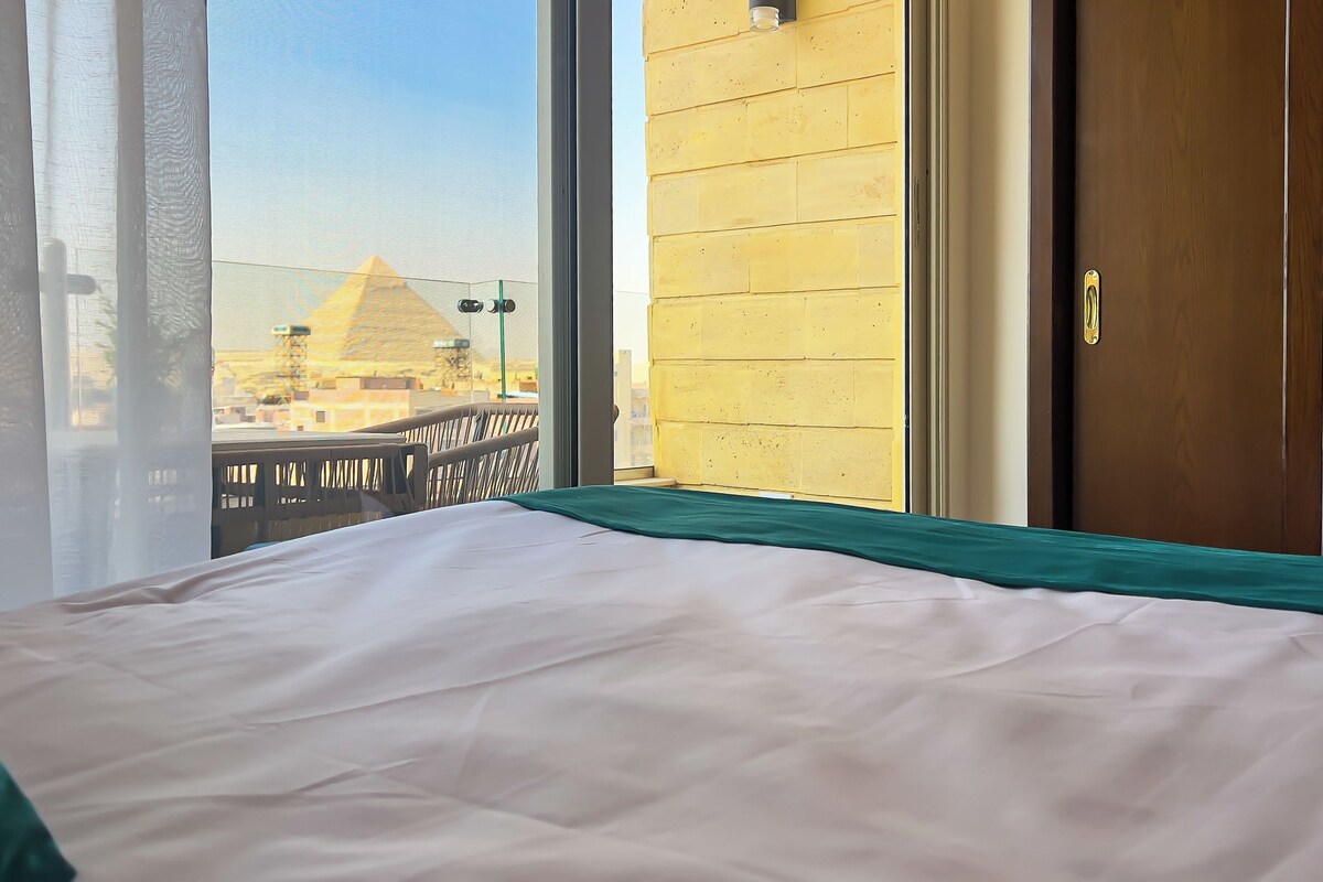 A hotel room with a bed, a view of a pyramid, and a wooden door.
