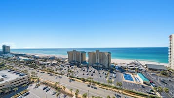 Un paysage urbain côtier avec un hôtel en bord de mer, des zones de stationnement et un ciel bleu dégagé.
